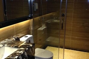 Un baño moderno con ducha de mampara de vidrio, lavamanos de mármol y un inodoro.