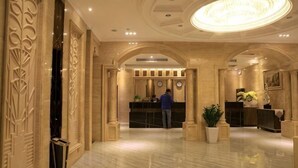 A hotel lobby with a reception desk, a clock, and a large chandelier. - Haihe Business Hotel (Enping)