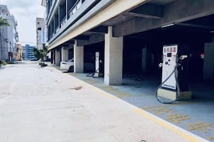 Un garaje para estacionar con pilares de hormigón, un coche blanco y una estación de carga.