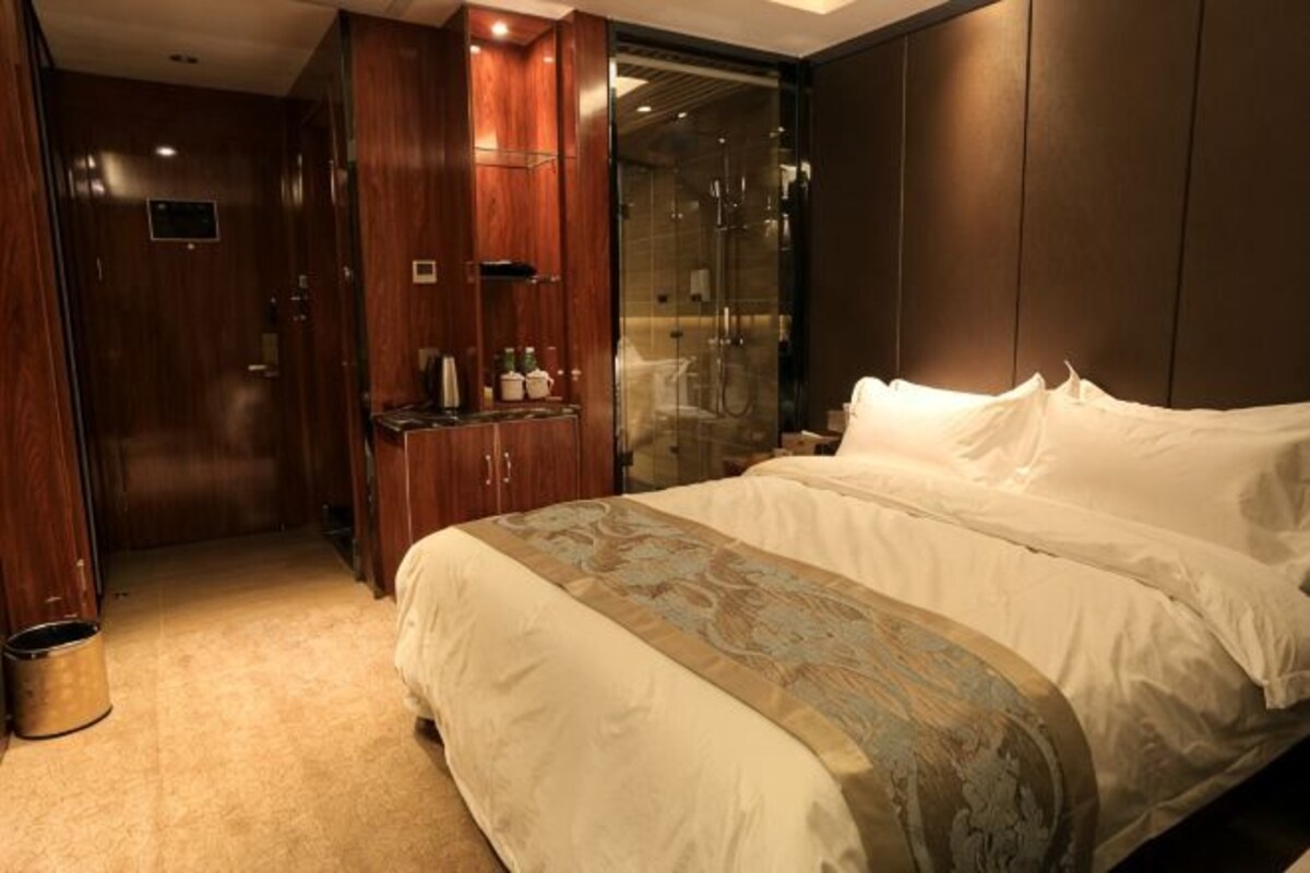Habitación de hotel con una cama grande, armario, espejo y zona de ducha.