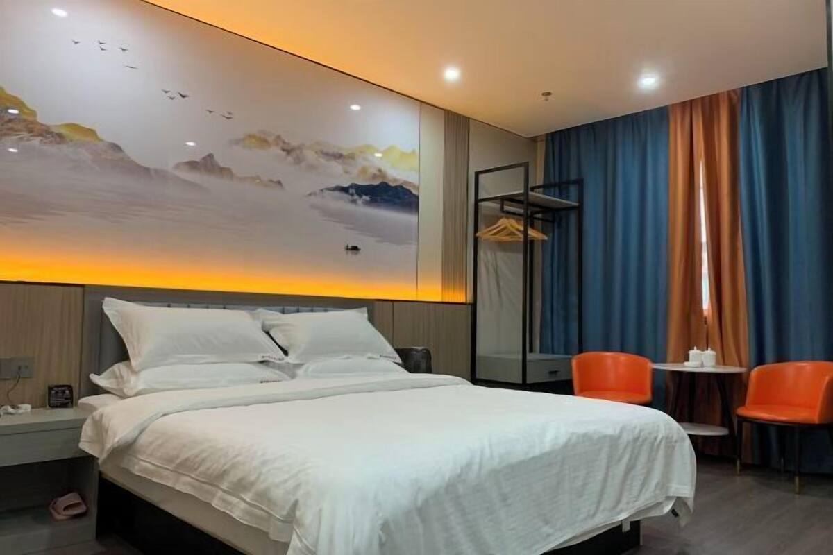 Una habitación de hotel con cama, mesita de noche, silla, mesa y un cuadro en la pared.