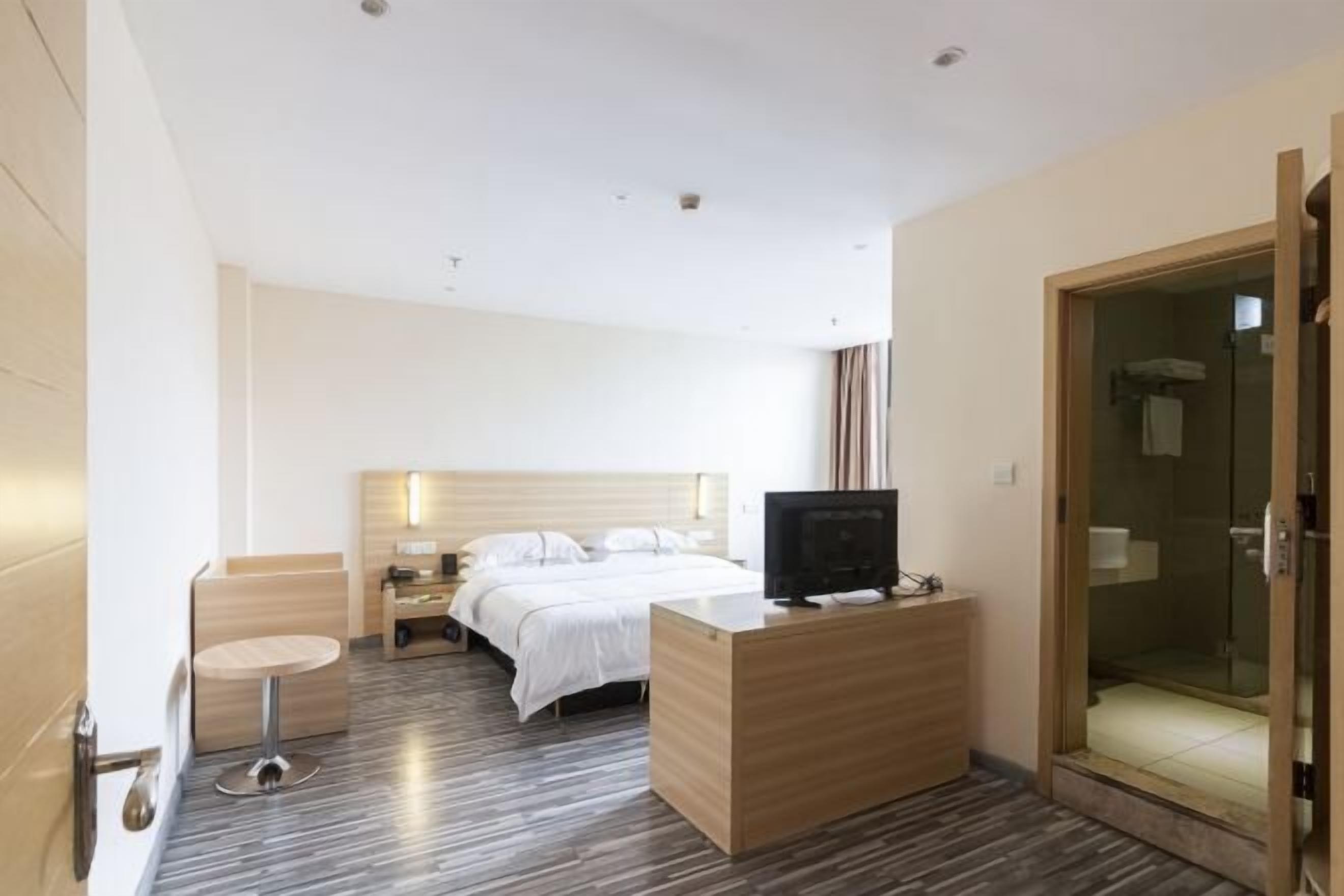 Habitación de hotel con cama, televisión, escritorio y zona de ducha.
