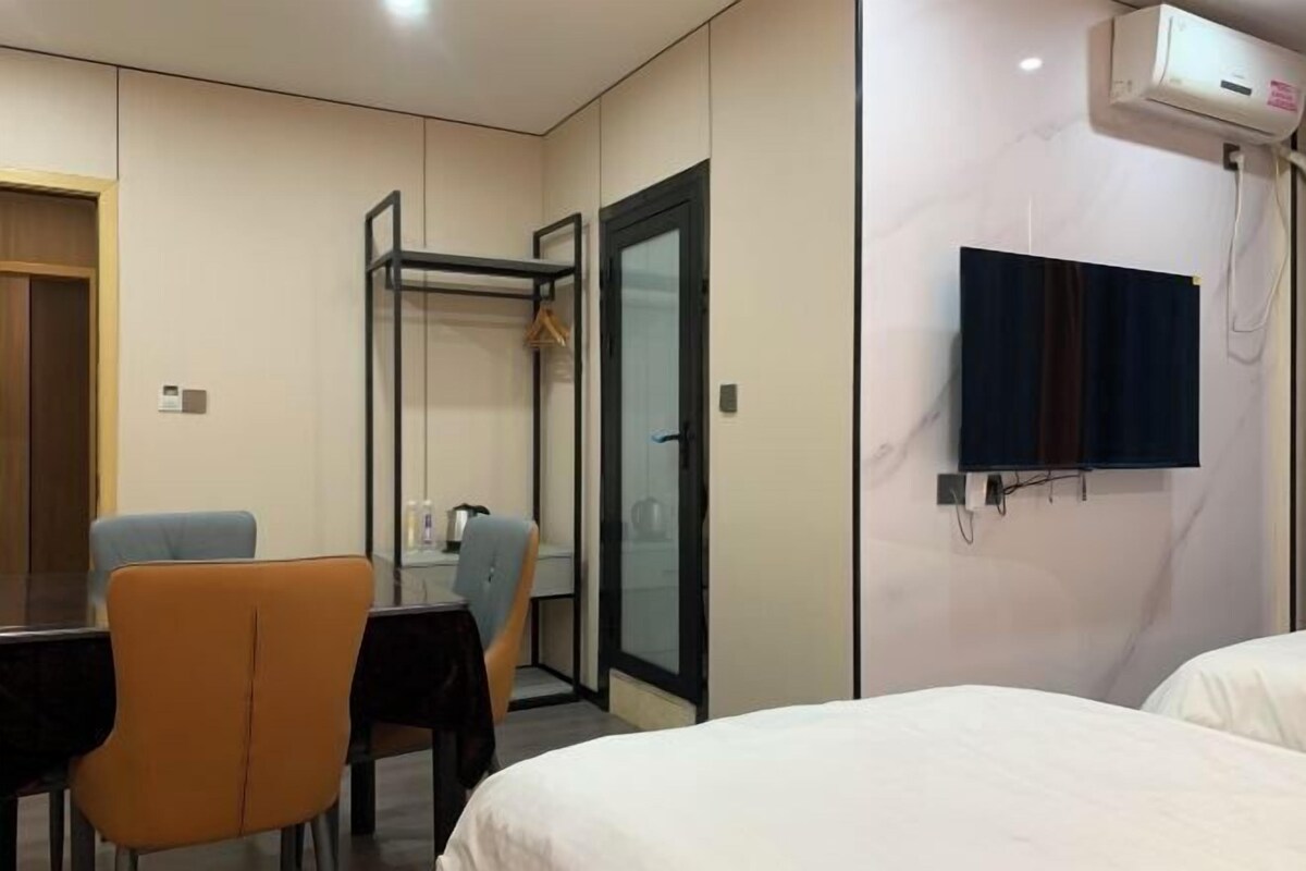 A hotel room with a bed, a desk, a chair, a TV, and an air conditioning unit.