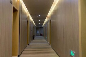 Un couloir d’hôtel avec des portes des deux côtés, un sol recouvert de moquette et un écran numérique fixé au mur.