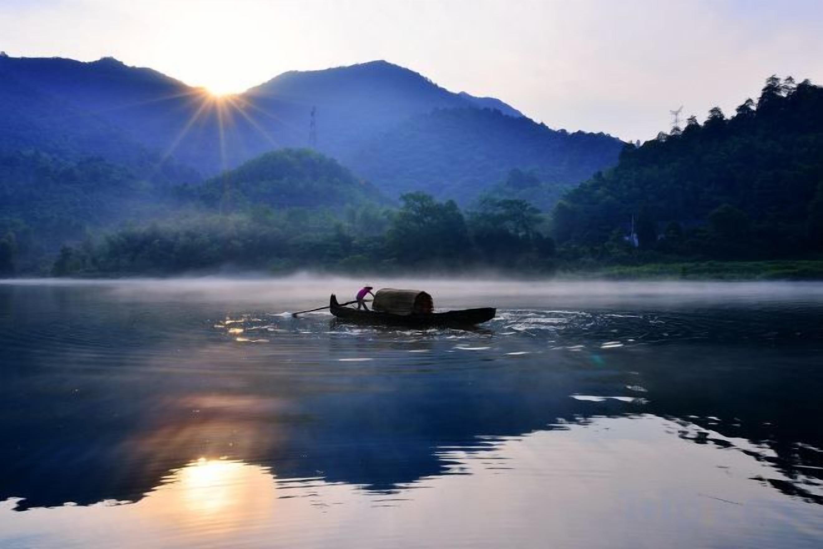 A calm body of water with a boat carrying a person and a container, surrounded by mist and mountains in the background.