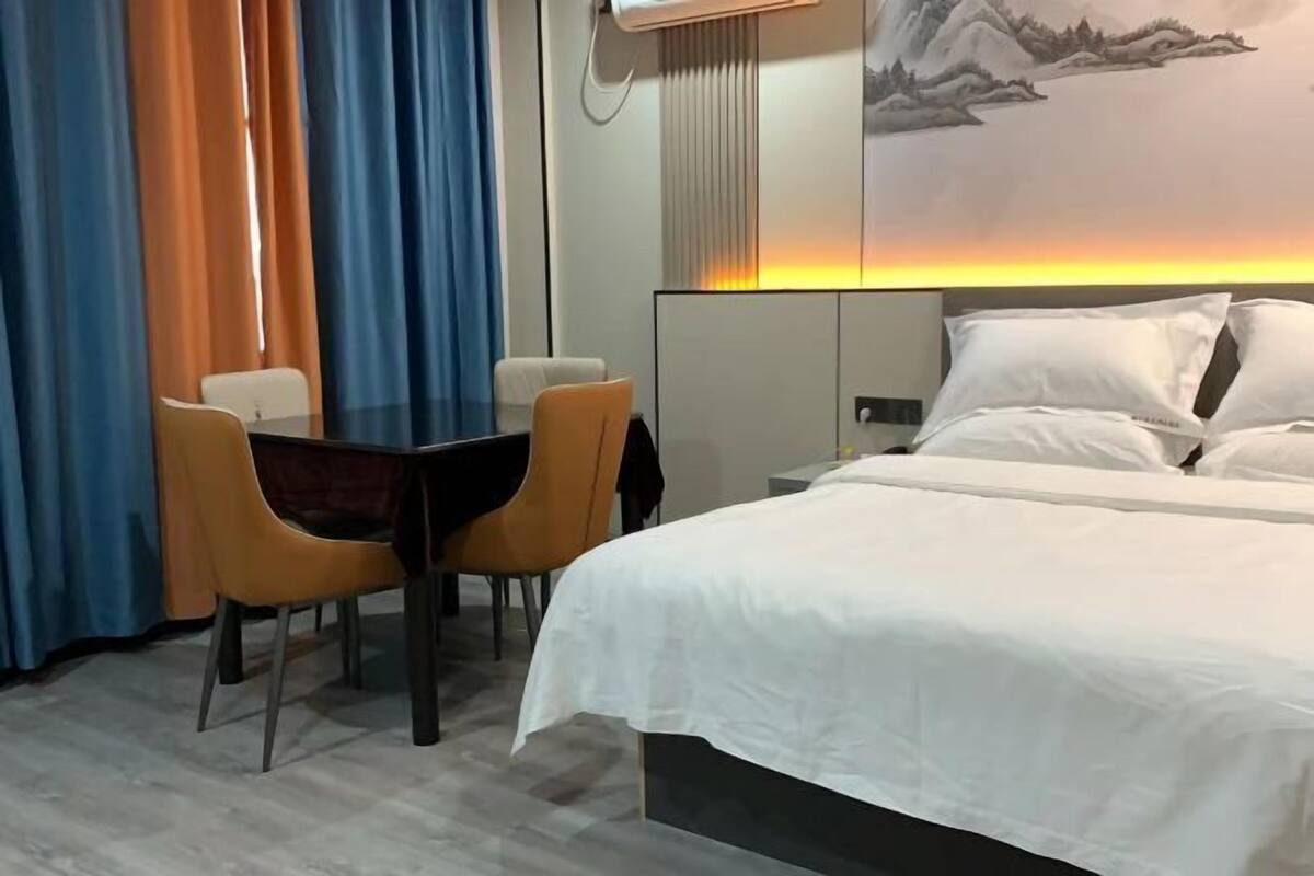 Una habitación de hotel con cama, un escritorio y dos sillas, un cuadro en la pared y cortinas.