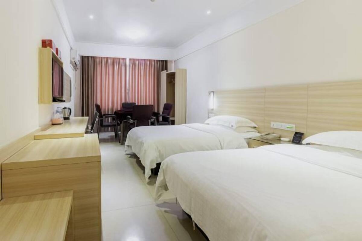 Habitación de hotel con dos camas, un escritorio, una silla y un televisor.