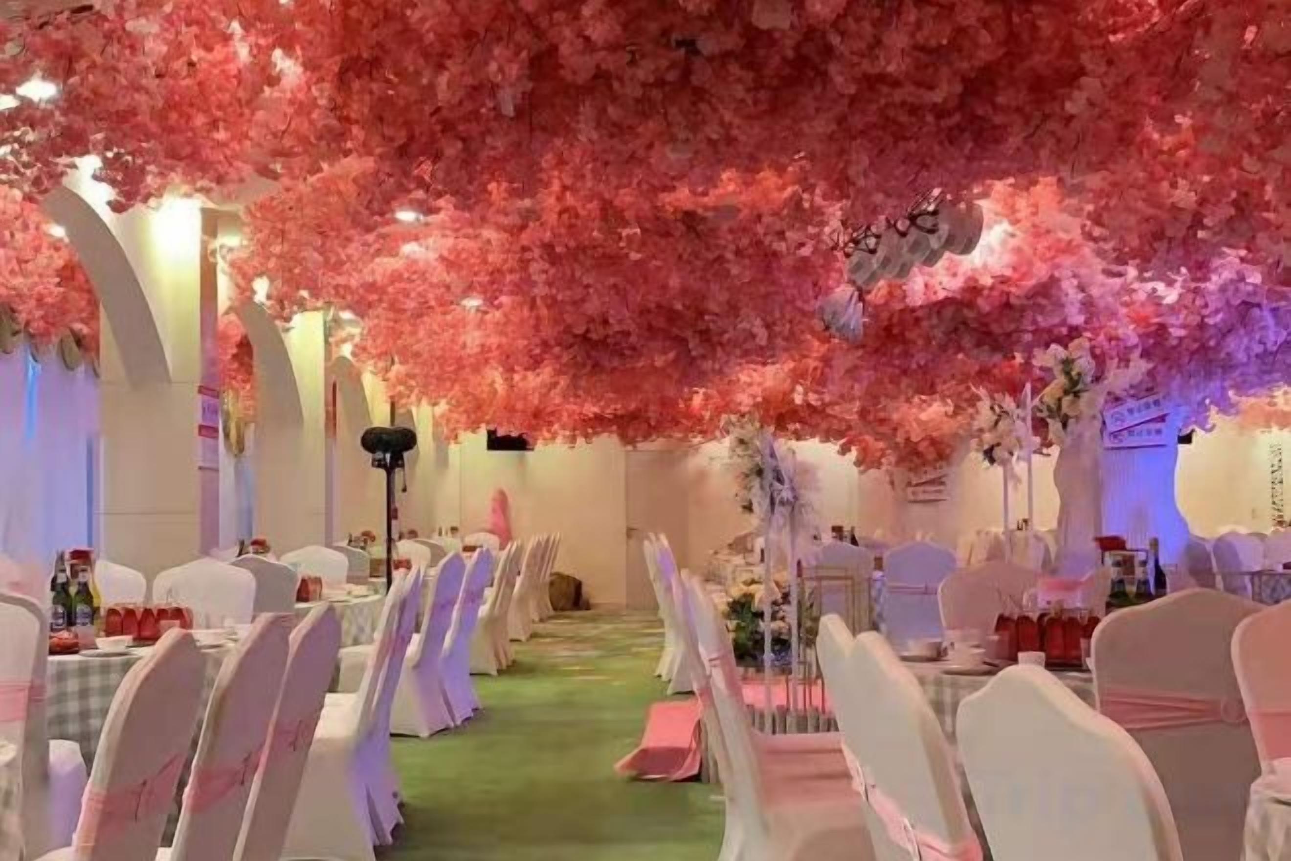 A banquet hall with rows of tables and chairs, a green carpet, and a floral canopy overhead.