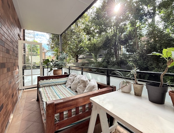 A balcony with a bed, a table, and potted plants.
