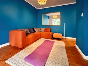 A living room with a sectional sofa, a small ottoman, a yoga mat, a mirror, and a floor lamp.