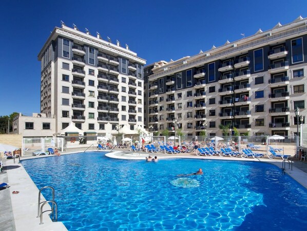 Un hôtel doté d’une grande piscine, entourée de chaises longues bleues et de parasols.
