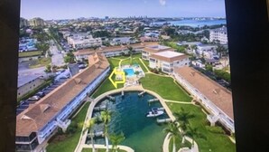 Vue aérienne d’une propriété située sur la côte, avec une piscine centrale, une végétation luxuriante et une marina.