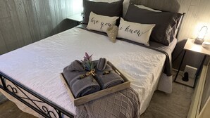 A neatly made bed with a tray of folded towels, a decorative pillow, and a bedside table with a lamp. - Romantic Cabin: Hot Tub, Pet friendly, 2m Whitewater, Concierge, Private driver (Canyon Lake)