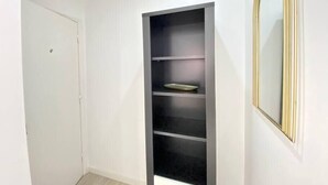 Une pièce avec une porte blanche, une étagère noire et un miroir à cadre doré.