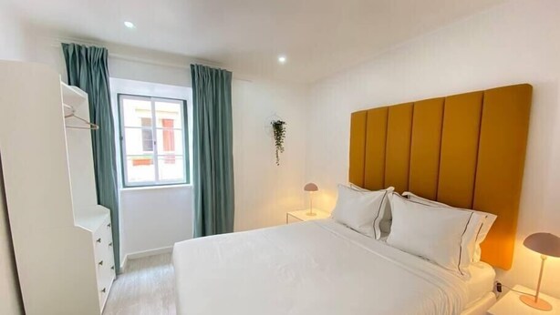 Une chambre d’hôtel avec un grand lit, une table de chevet avec une lampe, une armoire et une fenêtre avec des rideaux.