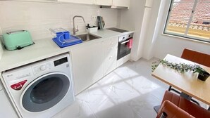 Une cuisine compacte avec des meubles blancs, un lave-linge encastré, un grille-pain et un évier.