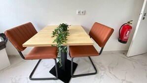 Une table à manger avec quatre chaises marron, une plante en pot et un extincteur accroché au mur.