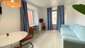 Un salon moderne avec un canapé bleu clair, une table ronde entourée de chaises et un téléviseur posé sur un meuble.