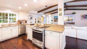 A spacious kitchen with white cabinetry, a large stove, and a dining area with a white sofa. - Charming Ranch w/spa, 1/2 acre near Miramar Beach (Montecito)