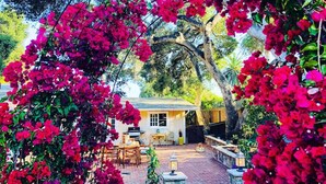 A house with a patio, surrounded by lush greenery and vibrant bougainvillea flowers. - Charming Ranch w/spa, 1/2 acre near Miramar Beach (Montecito)