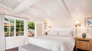A bedroom with a large bed, a bench, a nightstand, and a window with a view of greenery. - Charming Ranch w/spa, 1/2 acre near Miramar Beach (Montecito)