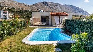 Ein Schwimmbad mit Blick auf eine Berglandschaft, eine kleine Terrasse mit einer Pergola und eine Rasenfläche mit Pflanzen.