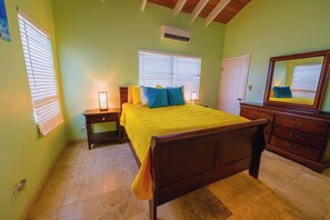 A bedroom with a bed, bedside tables, a dresser, a mirror, and a window with blinds. - Perfect 4BDRM for families or groups! (Frederiksted)