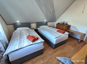 Cozy bedroom with two single beds, a wooden bench, and a nightstand with a lamp.
