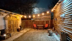 A covered outdoor area with a wooden table and chairs, string lights, and a stone wall.