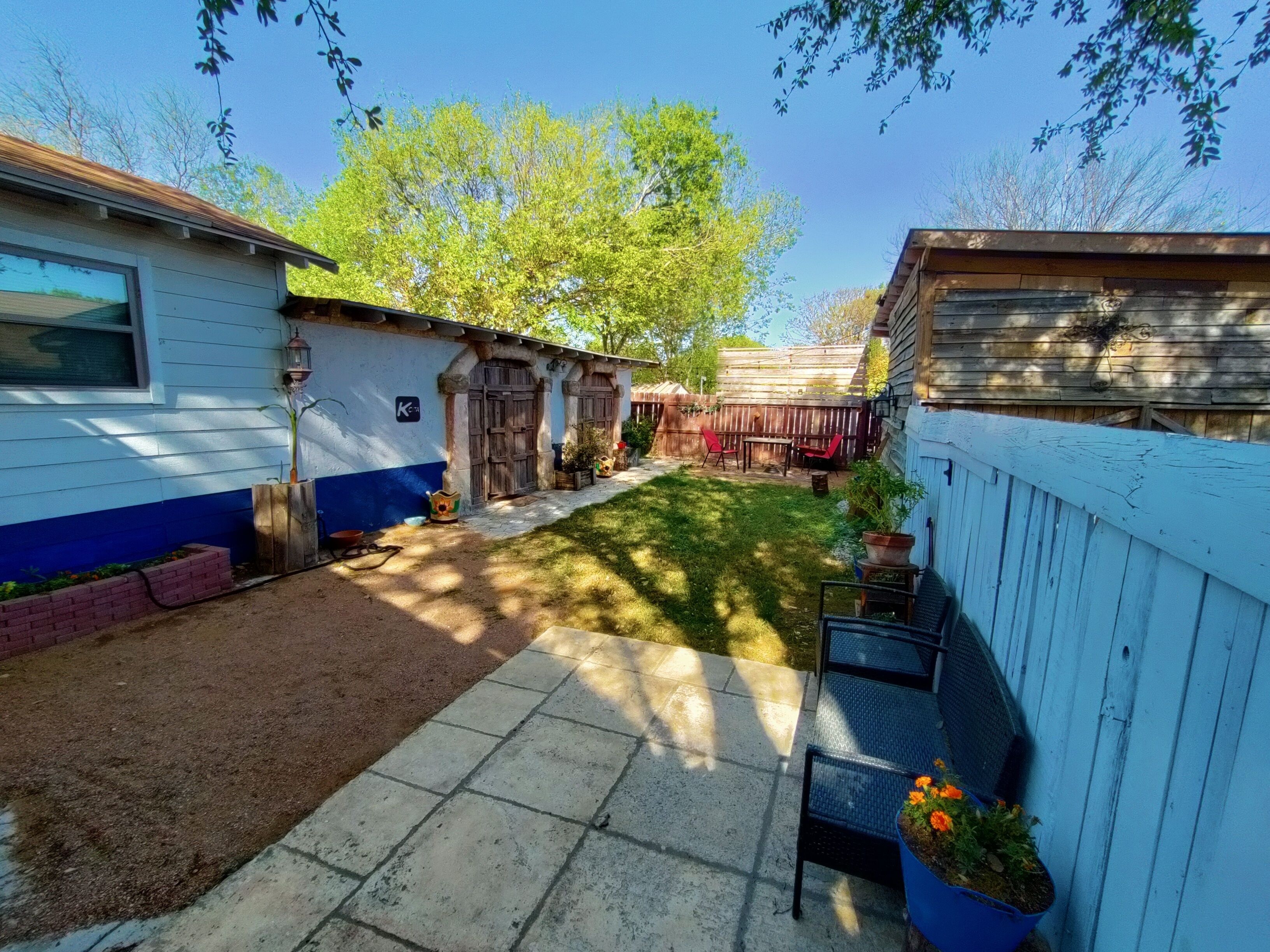 Un patio trasero con terraza de madera, una pequeña zona de patio y un jardín cercado.