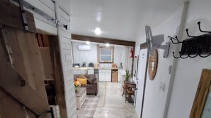 A narrow hallway leading to a living area with a sofa and a kitchen in the background.