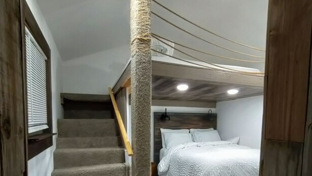 A bedroom with a bed, a wooden staircase, and a textured column.