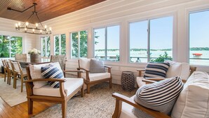 A spacious sunroom with large windows overlooking a body of water, wooden furniture, and a central chandelier. - Amazing Lake House - beautiful clear lake - 2 hours from Chicago! (Sturgis)