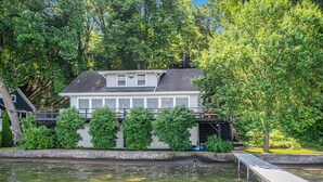 A house with a dock extending into a calm body of water, surrounded by lush greenery and trees. - Amazing Lake House - beautiful clear lake - 2 hours from Chicago! (Sturgis)