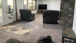 A living room with two armchairs, a flat-screen TV, and a stone fireplace. - Poskin Lake Getaway Cabin Lakefront access and beautiful sunrise (Almena)