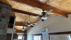 A room with wooden ceiling beams, a stone fireplace, and two ceiling fans. - Poskin Lake Getaway Cabin Lakefront access and beautiful sunrise (Almena)