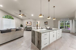 A spacious living area with a large island, a ceiling fan, and a view of the outdoors.