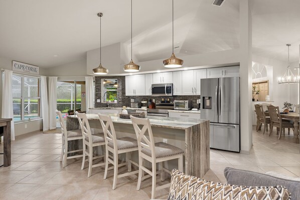 A modern kitchen with white cabinetry, stainless steel appliances, and a central island with seating.