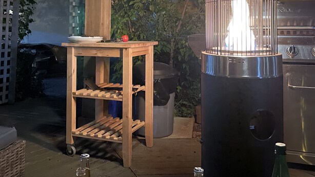 Une terrasse extérieure dotée d’une pergola en bois, une table avec une bouteille de bière Corona Extra et un barbecue portable dont on peut voir la flamme.