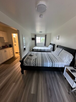 A bedroom with two beds, a small kitchenette, and a window with curtains.