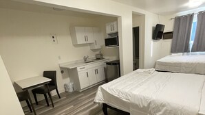 Une chambre d’hôtel avec deux lits, une petite table ronde, un coin cuisine et un bureau.
