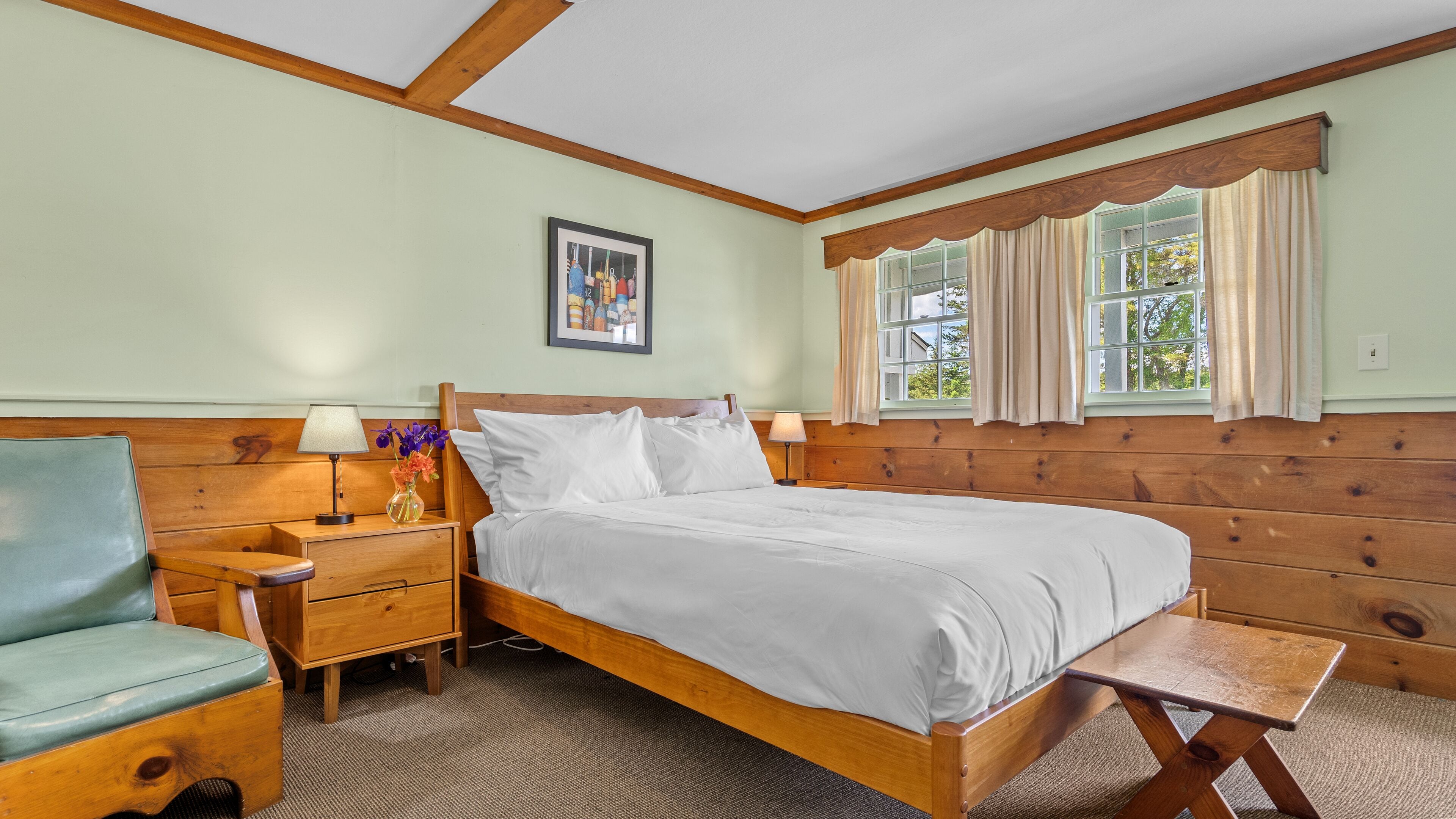 Um quarto com cama de madeira, mesa de cabeceira com abajur, uma cadeira e janela com cortinas.