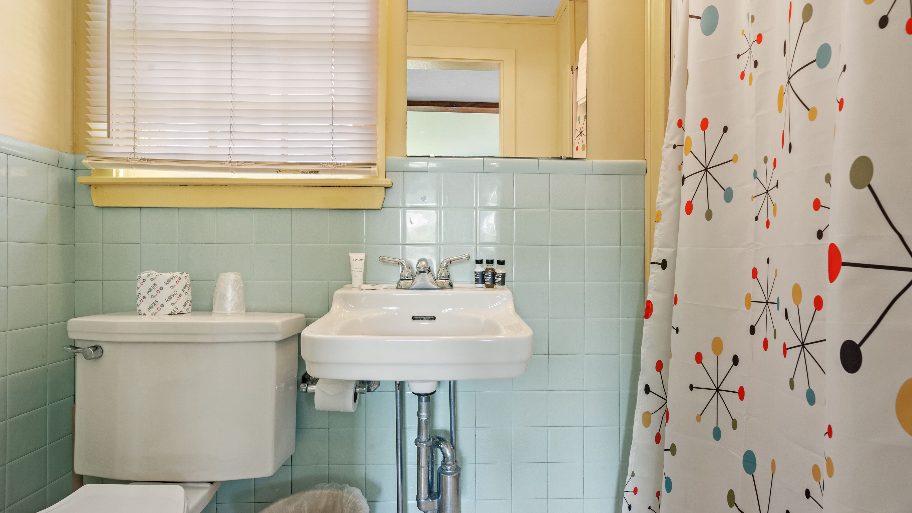 Een badkamer met toilet, wastafel en douchegordijn met een geometrisch patroon.