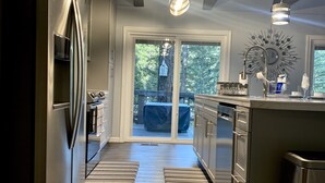 A modern kitchen with stainless steel appliances, a wooden floor, and a view of a deck with a table and chairs.