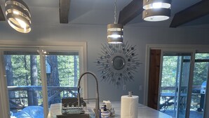 A kitchen with a large island, a sink, and a decorative mirror. There are overhead lights and a view of the outdoors.