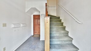 Una escalera con barandilla de madera y barandilla blanca a la derecha. Hay dos interruptores de luz y dos ganchos fijados a la pared.