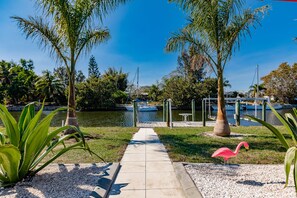 A pathway leading to a marina with boats docked, surrounded by palm trees and a flamingo statue. - NEW MODERN 4/3 WATERFRONT HEATED POOL GULF ACCESS FLORIDA HOME (Port Charlotte)