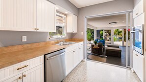 Une cuisine moderne avec des meubles blancs, un lave-vaisselle en acier inoxydable et un plan de travail en bois.