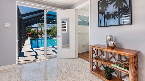 Un intérieur moderne avec une porte vitrée donnant sur une piscine, une console en bois et un tableau encadré représentant des palmiers.