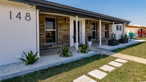 Une maison moderne, portant le numéro 148, qui se distingue par sa façade en pierre, ses nombreuses fenêtres et un jardin bien entretenu, agrémenté de plantes et de pierres de pas.